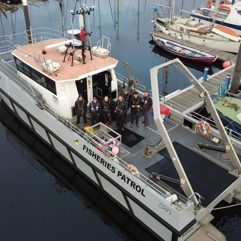 Fisheries patrol boat docked in marina, with NIFCA officers on deck.