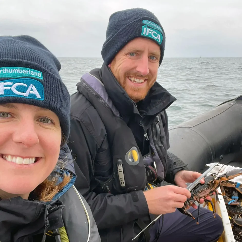 Two NIFCA members wearing branded beanies at sea during a lobster V-notching exercise.