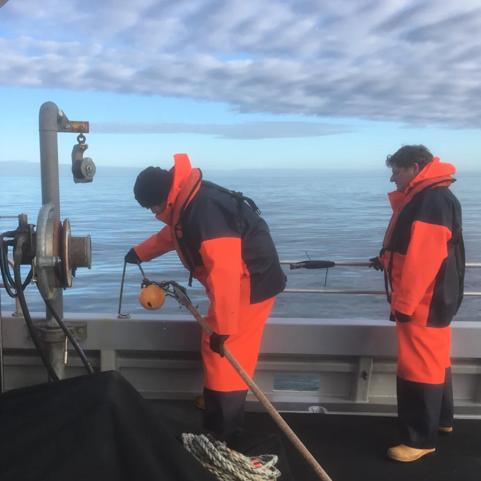 Two NIFCA staff in orange hi-vis workwear on a boat.