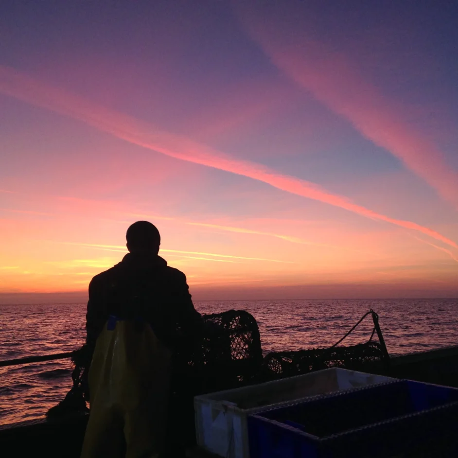 Stunning pink sky in Northumberland with silhouette of fisherman at sea.