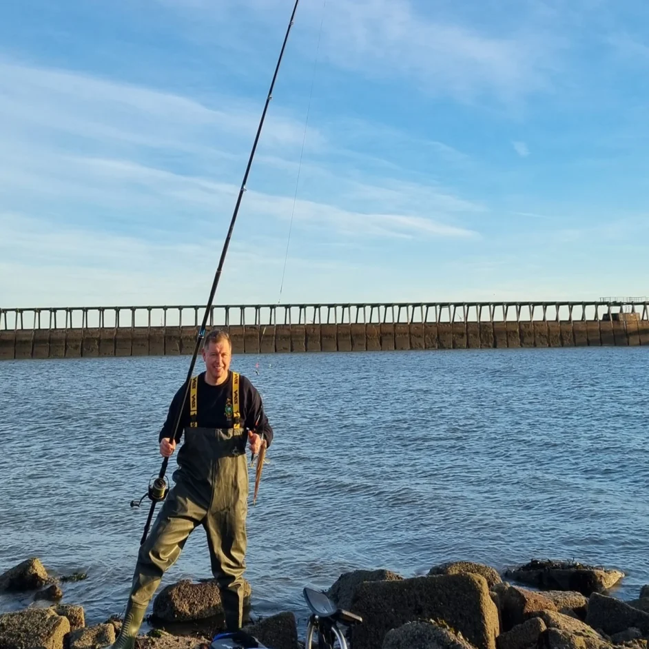 Angler smiling with catch on Northumberland shoreline.
