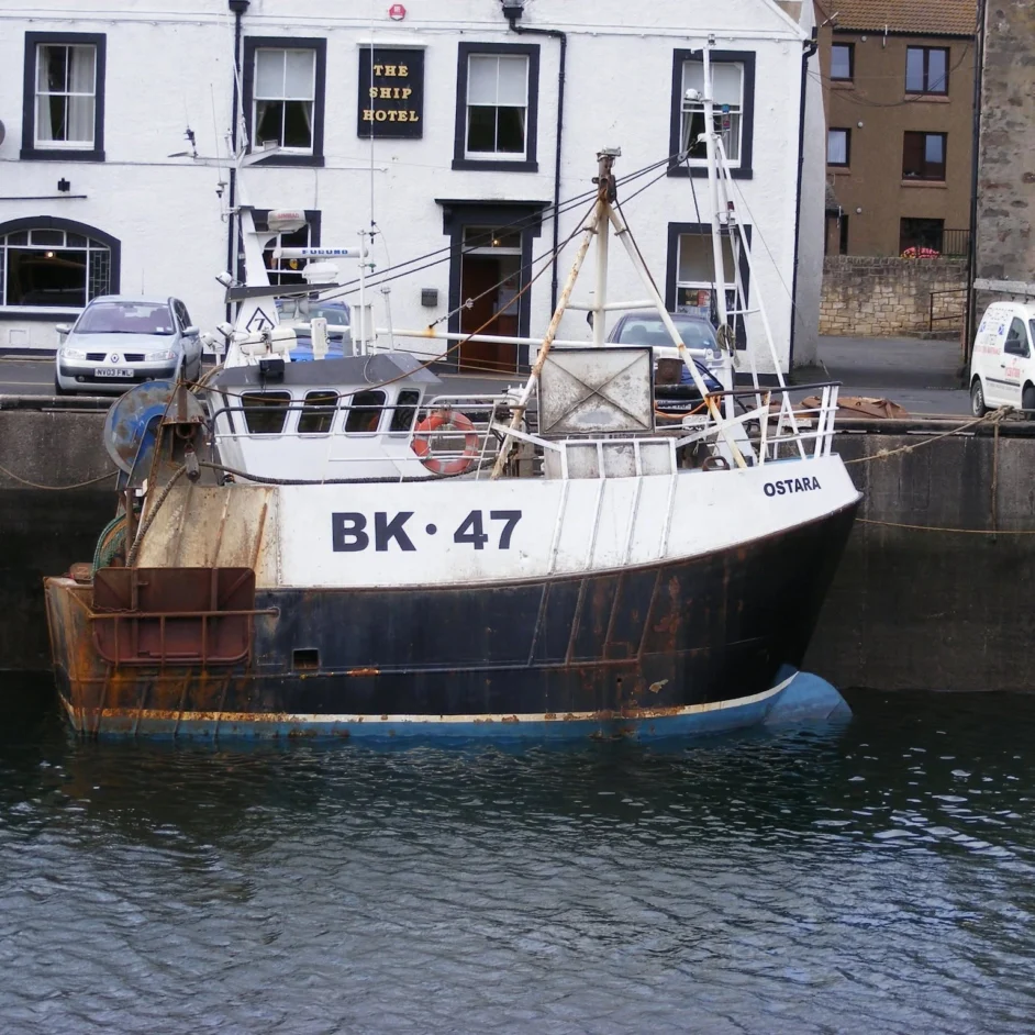 A traditional commercial fishing boat, the Ostara (BK 47), moored along a concrete harbour.
