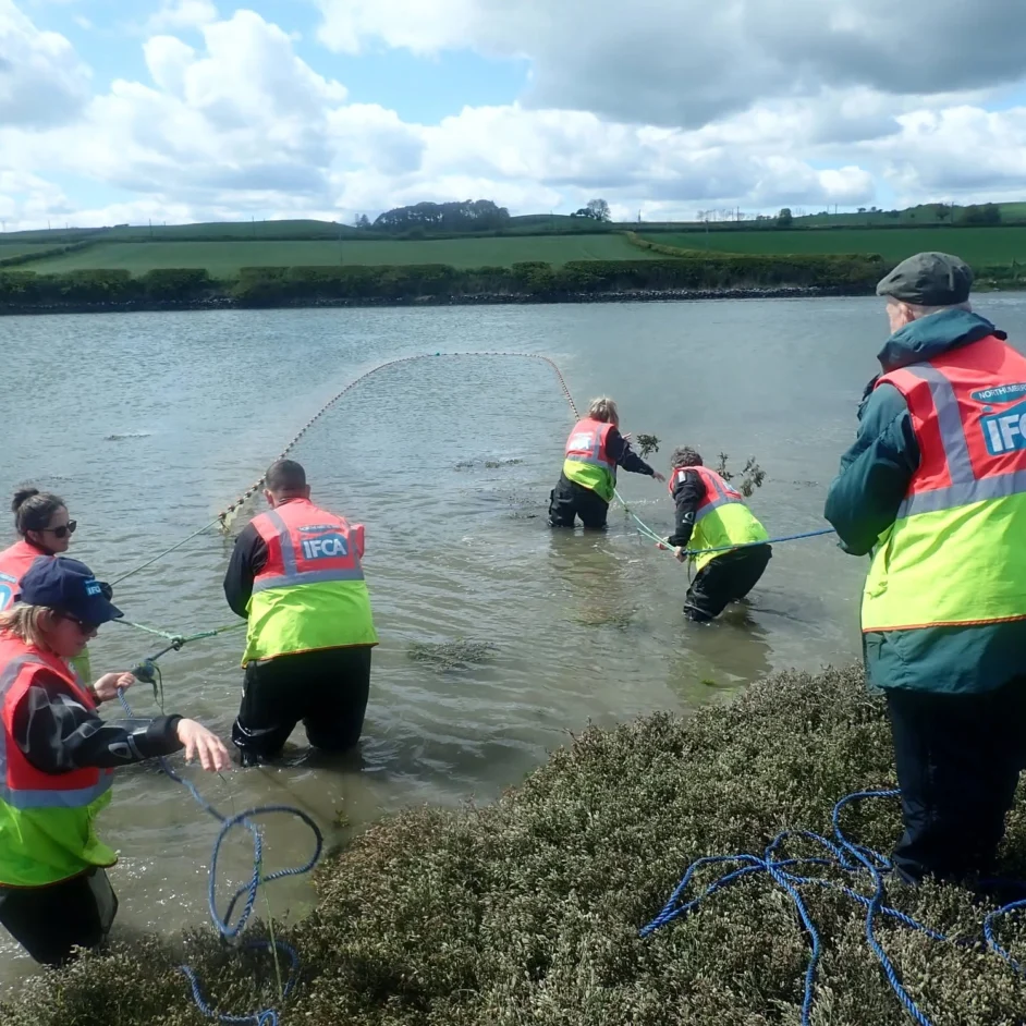 NIFCA officers in hi-vis throwing nets into water during survey.
